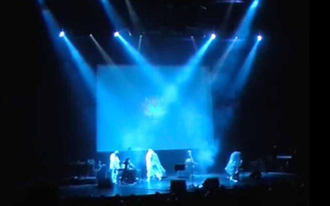 The band Coil live on stage at the Barbican. Four figures on stage saturated by blue light.